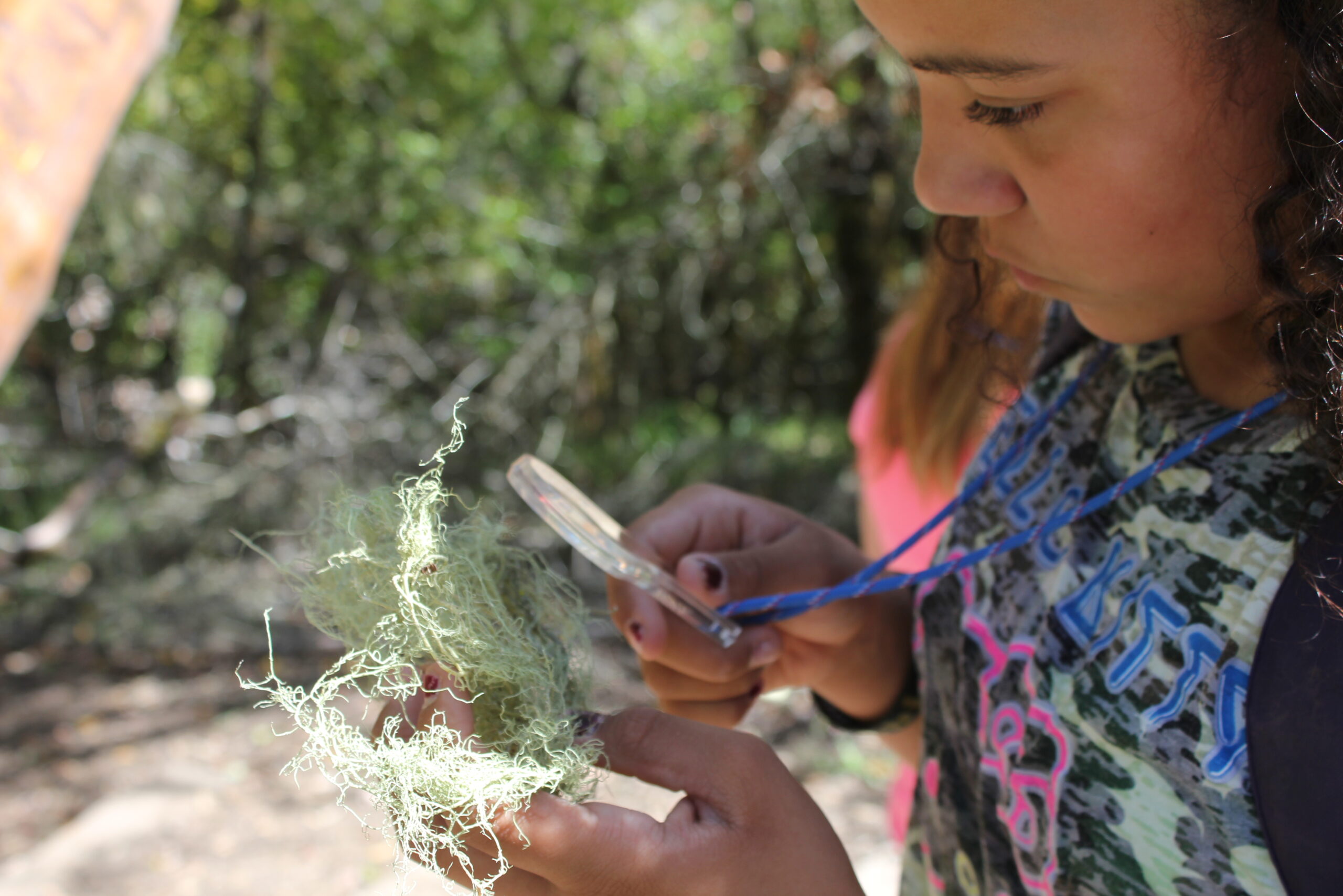 A student is outdoors examining nature through a hand lens